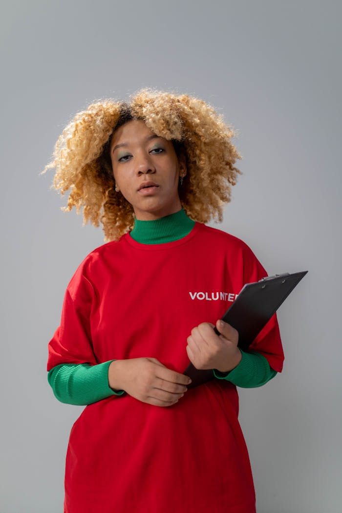 Young volunteer woman with curly hair holding a clipboard in a studio setting.