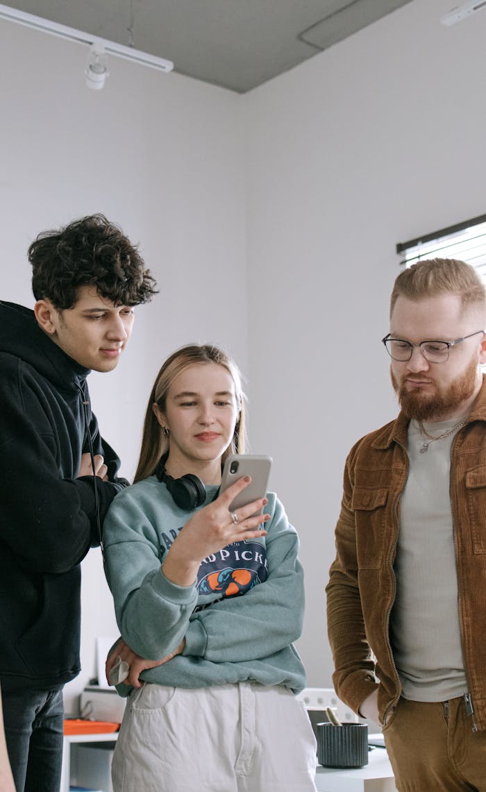 Three young professionals discuss work while interacting with a smartphone in a modern office setting.